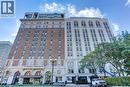 Grand multi-story building featuring a brick and stone facade, arched entryway with awnings, and a contemporary penthouse addition - 112 King Street E Unit# Ph6, Hamilton, ON 