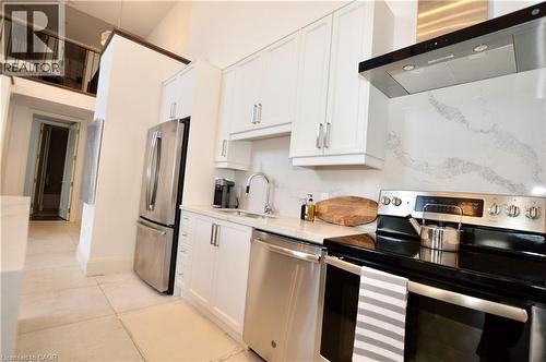 Modern kitchen featuring white cabinetry, stainless steel appliances, a white patterned backsplash, a stainless steel range hood, and light-toned tile flooring - 112 King Street E Unit# Ph6, Hamilton, ON - Indoor Photo Showing Kitchen With Stainless Steel Kitchen