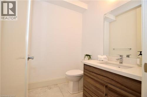 Contemporary powder room featuring a wood-finish vanity with a white countertop and integrated sink, chrome faucet, and a large wall-mounted mirror - 112 King Street E Unit# Ph6, Hamilton, ON - Indoor Photo Showing Bathroom