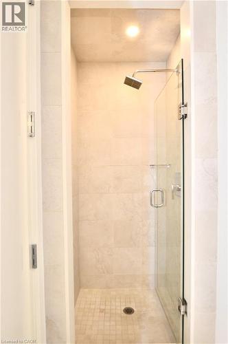 Walk-in shower featuring light-toned tile walls and floor, a glass enclosure, a ceiling-mounted light fixture, and a rain showerhead - 112 King Street E Unit# Ph6, Hamilton, ON - Indoor Photo Showing Bathroom