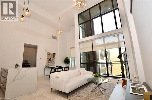 Two-story window wall with roller shades, high ceilings with pendant lighting, a kitchen island with a waterfall countertop and integrated wine storage, and light-toned tile flooring - 112 King Street E Unit# Ph6, Hamilton, ON - Indoor