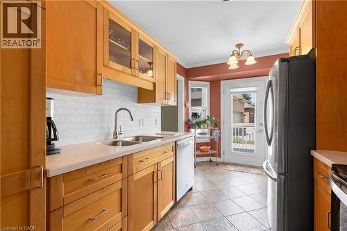 Kitchen featuring wood cabinetry, light-toned countertops, a white subway tile backsplash, a stainless steel double basin sink with a gooseneck faucet, and ceramic tile flooring - 50 Spadara Drive, Hamilton, ON 