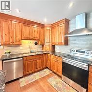 Full kitchen featuring wood cabinetry, dark countertops, subway tile backsplash, stainless steel appliances, and recessed lighting - 