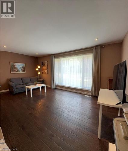 Spacious living area featuring rich wood-finish flooring, recessed lighting, and a large picture window with sheer and blackout drapes - 82 Blackwood Crescent, Hamilton, ON 