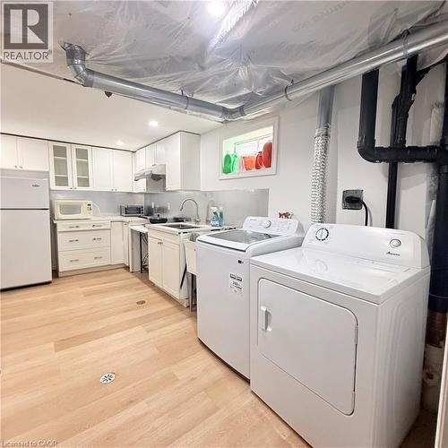 Full-size washer and dryer appliances, light wood-finish flooring, white cabinetry, recessed lighting, and a utility sink - 82 Blackwood Crescent, Hamilton, ON 