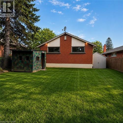 Spacious backyard with a large lawn, red brick exterior, side shed, and mature trees - 82 Blackwood Crescent, Hamilton, ON 