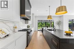 Gourmet kitchen featuring a built-in gas range, a dark range hood, light wood-finish flooring, white upper cabinetry, and a dark stone-finish island with integrated sink - 