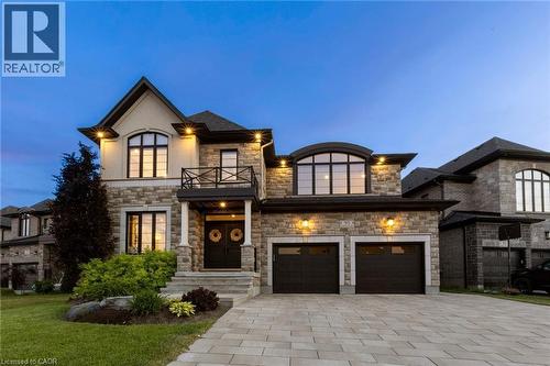 Stone and brick exterior with architectural lighting, arched windows, an over-sized two-car garage, a paver driveway, and a second-storey balcony - 95 Pondcliffe Drive, Kitchener, ON 