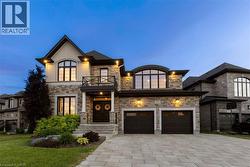 Stone and brick exterior with architectural lighting, arched windows, an over-sized two-car garage, a paver driveway, and a second-storey balcony - 