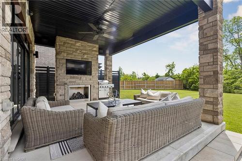 Oversized patio doors from the kitchen leading to the covered outdoor patio featuring stone columns, a built-in fireplace, SUNBRITE TV and a ceiling fan, overlooking the protected greenspace. - 95 Pondcliffe Drive, Kitchener, ON 