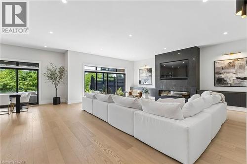 Spacious living room featuring media wall with integrated TV and electric fireplace clad in floor to ceiling quartz stone,designer light fixtures, 2 sets of oversized patio doors - 95 Pondcliffe Drive, Kitchener, ON 