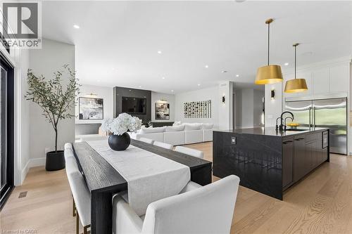 Open-concept interior featuring light wood-finish flooring, a dark waterfall island with a black faucet, white upper cabinetry, and stainless steel French door refrigerators - 95 Pondcliffe Drive, Kitchener, ON 