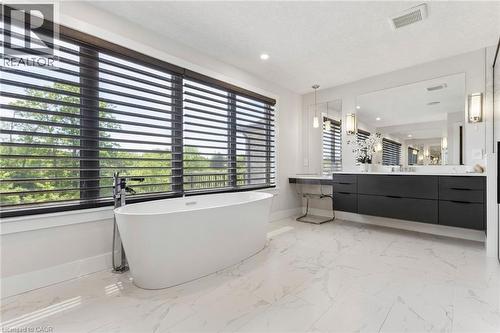 Freestanding soaking tub with a floor-mounted faucet, set against a wide window with horizontal blinds - 95 Pondcliffe Drive, Kitchener, ON 