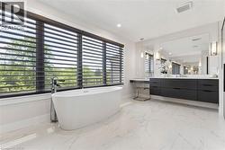 Freestanding soaking tub with a floor-mounted faucet, set against a wide window with horizontal blinds - 