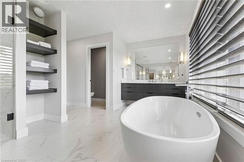 Bathroom featuring a freestanding oval tub, marble-look floor tiling, a dual-sink vanity with dark cabinetry, and built-in shelving - 95 Pondcliffe Drive, Kitchener, ON 