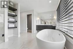 Bathroom featuring a freestanding oval tub, marble-look floor tiling, a dual-sink vanity with dark cabinetry, and built-in shelving - 
