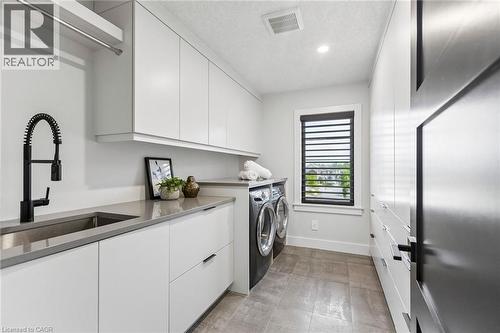 Modern utility room featuring extensive white cabinetry, a built-in sink with a matte black gooseneck faucet, light grey countertops, and tile flooring - 95 Pondcliffe Drive, Kitchener, ON 