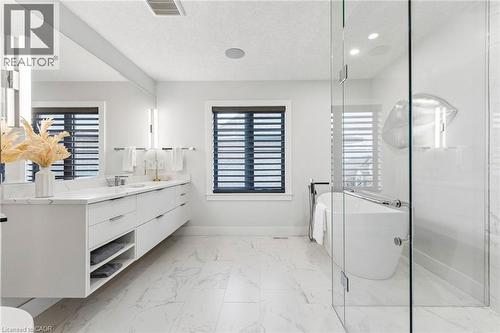 Designer bathroom featuring a floating dual-sink vanity with white countertop, full-width mirror, freestanding soaking tub, and an oversized curbless glass-enclosed shower - 95 Pondcliffe Drive, Kitchener, ON 