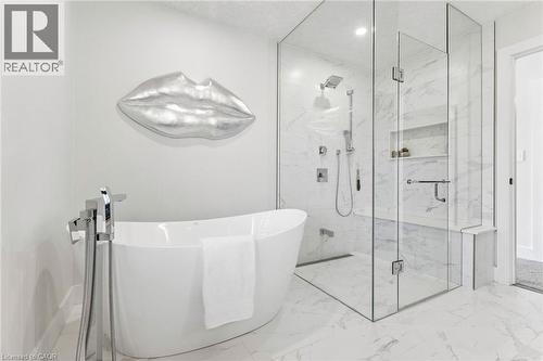 Freestanding tub with a floor-mounted tub-filler, frameless glass shower enclosure, built-in shower bench, and recessed shower niche, all set on marble-look tile flooring - 95 Pondcliffe Drive, Kitchener, ON 