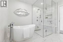 Freestanding tub with a floor-mounted tub-filler, frameless glass shower enclosure, built-in shower bench, and recessed shower niche, all set on marble-look tile flooring - 
