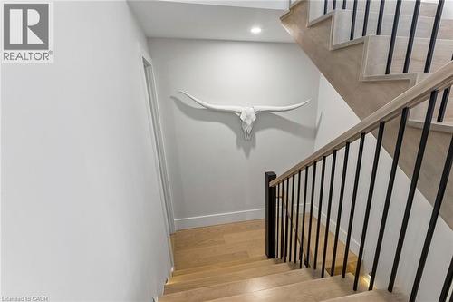 Custom waterfall staircase featuring light oak wood treads, black metal balusters, and matching natural wood handrail with low-voltage lighting - 95 Pondcliffe Drive, Kitchener, ON 