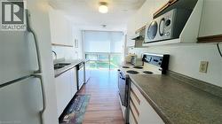 Galley kitchen featuring wood-finish flooring, white cabinetry, integrated appliances, a double basin sink, and ample countertop space - 