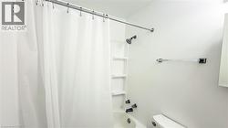 Shower/tub combination featuring a dark-finish showerhead and faucet fixtures, integrated shelving, and a white shower curtain - 