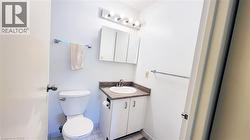 Bathroom featuring a white toilet, a vanity with a speckled countertop and integrated sink, a wall-mounted medicine cabinet, and a five-bulb vanity light fixture - 