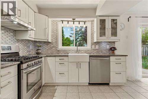 Modern kitchen featuring white cabinetry, stainless steel appliances, a white farmhouse sink, and granite countertops - 17 Piper Place, Caledonia, ON 