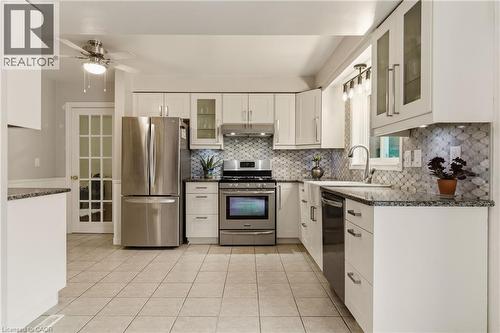 Kitchen featuring extensive white cabinetry, stainless steel appliances, granite countertops, patterned tile backsplash, and light-toned floor tiling - 17 Piper Place, Caledonia, ON 