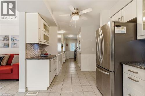 Kitchen featuring stainless steel refrigerator, white cabinetry, granite-finish countertops, mosaic tile backsplash, and tile flooring - 17 Piper Place, Caledonia, ON 