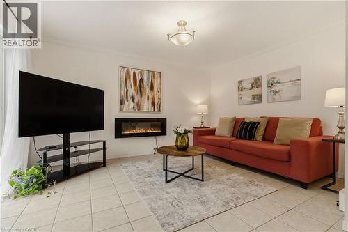 Living room featuring a wall-mounted electric fireplace, neutral tile flooring, crown molding, and a semi-flush mount ceiling light - 17 Piper Place, Caledonia, ON 