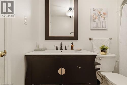 Bathroom vanity featuring a dark wood-finish cabinet with circular pulls, an integrated white sink, and a dark-framed mirror - 17 Piper Place, Caledonia, ON 