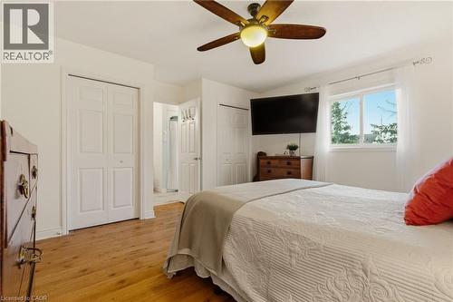 Bedroom featuring wood-finish flooring, a ceiling fan with integrated lighting, a double window with white sheers, and two white bi-fold closet doors - 17 Piper Place, Caledonia, ON 
