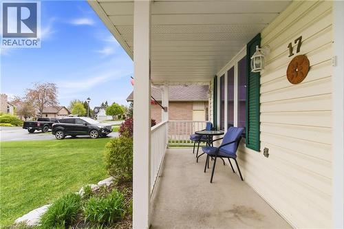 Covered front porch with white railings and beige siding, featuring green window shutters and a visible house number - 17 Piper Place, Caledonia, ON 