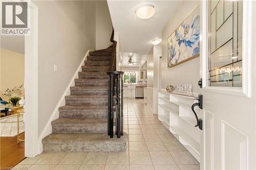Entryway featuring ceramic tile flooring, a carpeted staircase with dark wood banister, and built-in shelving - 17 Piper Place, Caledonia, ON 