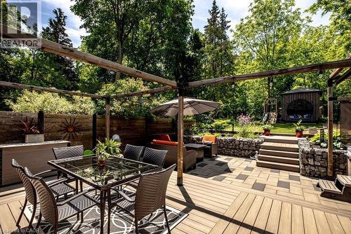 Multi-level outdoor living space featuring a wood-finish deck, stone retaining walls, and a separate paved patio area - 99 Hillcrest Avenue, Hamilton, ON 