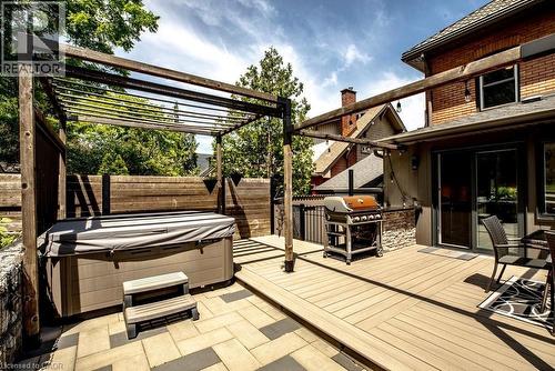 Outdoor living space featuring a wood-finish pergola, a built-in spa, composite decking, a paver patio, and sliding glass door access to the interior - 99 Hillcrest Avenue, Hamilton, ON 
