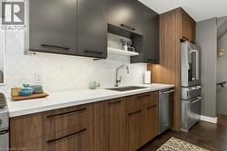 Contemporary kitchen featuring two-tone cabinetry with dark upper cabinets and wood-finish lower cabinets, light-toned countertops, and a patterned tile backsplash - 