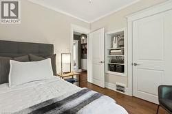 Bedroom featuring wood-finish flooring, crisp white trim, and a built-in shelving nook with patterned backing - 