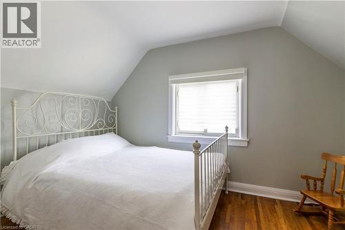 Interior room featuring hardwood flooring, a window with blinds, light gray walls, white trim, and an angled ceiling - 20 West 1St Street, Hamilton, ON 