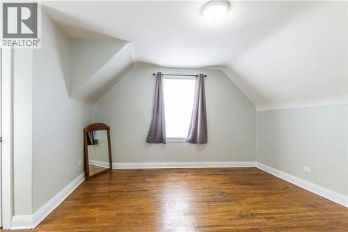 Room featuring sloped ceilings, hardwood flooring, a single window, and a flush mount ceiling light fixture - 20 West 1St Street, Hamilton, ON 