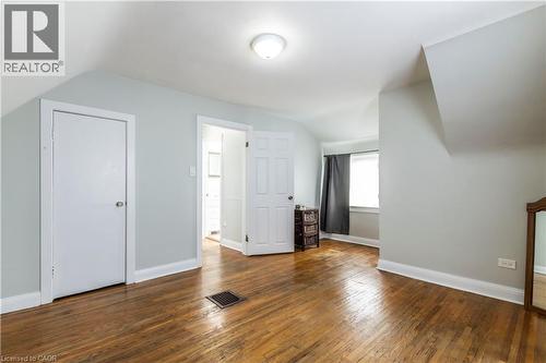 Attic room featuring wood-finish flooring, light-colored walls, sloped ceilings, and a window with dark curtains - 20 West 1St Street, Hamilton, ON 