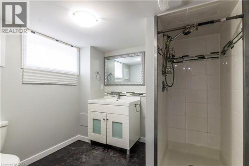 Full bathroom featuring a walk-in shower with tile surround, a white vanity with frosted glass cabinet doors, a rectangular undermount sink, and a framed vanity mirror - 20 West 1St Street, Hamilton, ON 