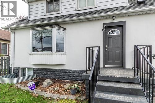 Exterior facade featuring a dark gray paneled entry door with an arched glass insert, flanked by black metal handrails - 20 West 1St Street, Hamilton, ON 