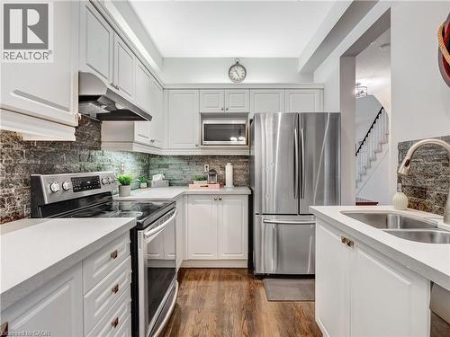 Modern kitchen featuring white cabinetry, light-colored countertops, a textured dark stone backsplash, stainless steel appliances, and wood-finish flooring - 2229 Walkers Line Unit# 6, Burlington, ON - Indoor Photo Showing Kitchen With Stainless Steel Kitchen With Double Sink With Upgraded Kitchen