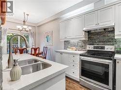 Kitchen featuring white cabinetry, a dual basin stainless steel sink with a gooseneck faucet, light-toned countertops, and a dark stone backsplash - 