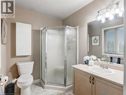 Shower enclosure with frosted glass and chrome trim, vanity with laminate countertop and integrated sink, light wood-finish cabinetry, tile flooring, and a large wall-mounted mirror - 