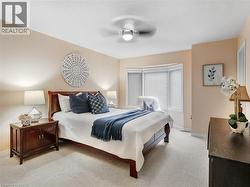 Bedroom featuring a bay window with blinds, a ceiling fan with integrated lighting, and neutral carpeting - 