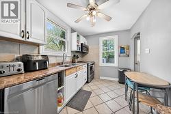 Kitchen featuring white cabinetry, light-toned countertops, a stainless steel dishwasher, and tile flooring - 